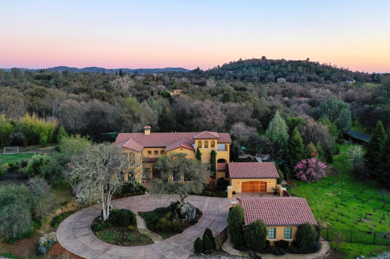 Aerial view of a luxury villa surrounded by lush greenery and hills during sunset.