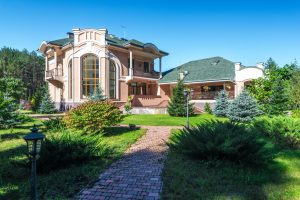 Property 2 Beautiful mansion in sunny weather, surrounded by lush greenery and a clear blue sky.